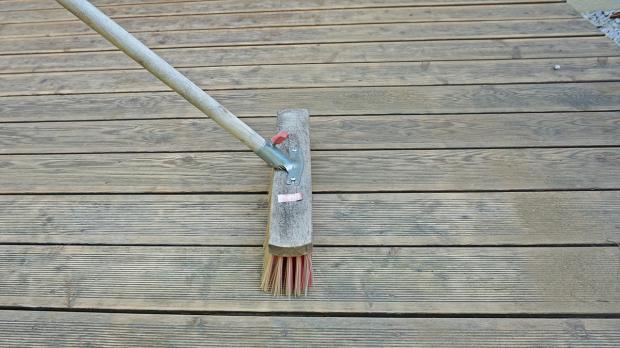 Holzbohlen der Terrasse mit Besen reinigen